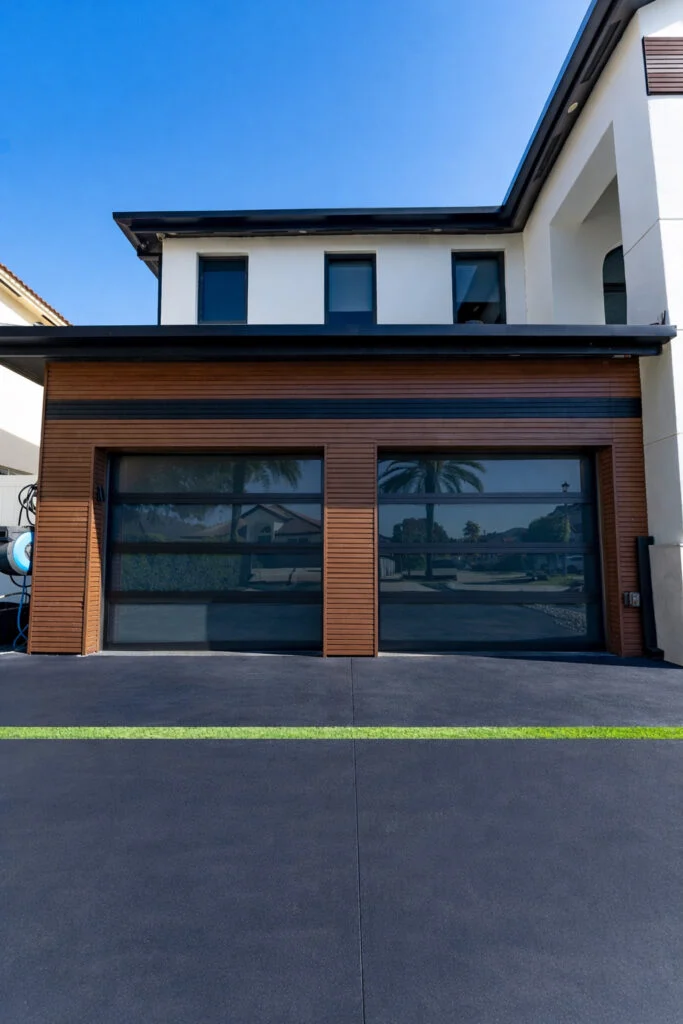 Two Dubai Framed glass garage doors with bronze frames and grey glass with a white interlayer in wood-slat cladding