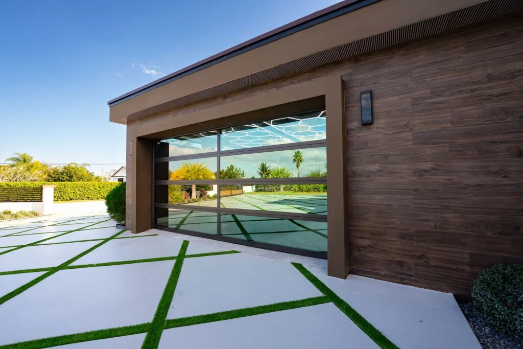 Two-car Dubai Framed glass garage door with black aluminum frames in a wood-clad modern garage beside a turf-strip driveway