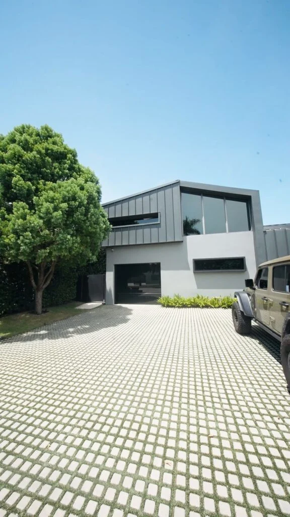 Grass-paver driveway leading to a modern home with a Dubai Frameless black glass garage door