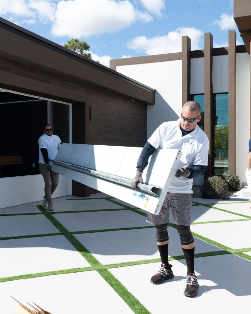 Two installers carrying a glass door section across the driveway
